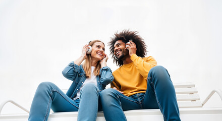 Two friends sharing headphones while sitting on a bench and smiling