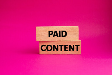 Paid content message written on wooden blocks on pink background. Conceptual paid content symbol. Copy space.