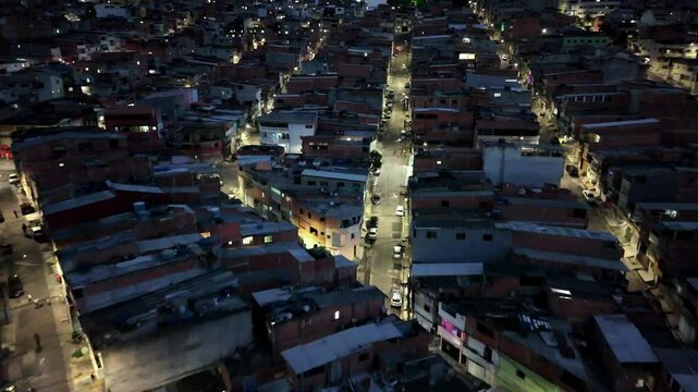 Aerial top-down shot of urban streets in a S&atilde;o Paulo favela at night, with glowing lights, narrow alleys, and compact housing in Osasco, Brazil.