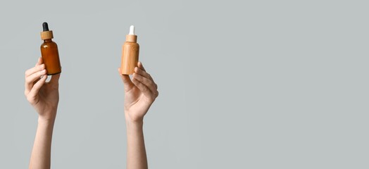 Hands holding bottles of essential oil on grey background with space for text