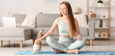 Young woman with cute kitten sitting on yoga mat at home © Pixel-Shot