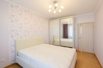 bedroom features a bed, wallpaper, mirrored closet, and door. A light fixture is centered on the ceiling, illuminating the space