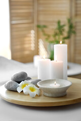 Burning candles with stones and flowers on couch in spa salon, closeup