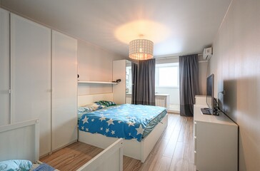 cozy bedroom featuring a bed with a blue star-patterned blanket, white wardrobes, a TV, a window...