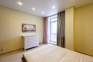 cozy bedroom with a bed, white dresser, and a painting on the wall. The room features warm yellow walls and curtains flanking a window