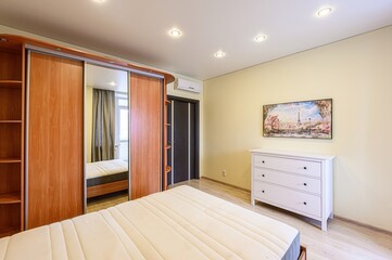 bright bedroom featuring a bed, wooden wardrobe with mirrors, white dresser, and a painting of Paris