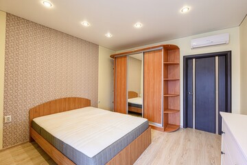 well-lit bedroom features a bed, sliding door wardrobe, and floral wallpaper. There's a door and air conditioner unit visible