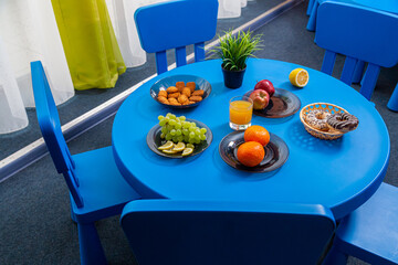 The children's cafe has a blue round table with fruits, juice, cakes and plants on it