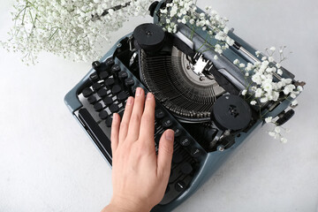 Female hand with vintage typewriter and flowers on white grunge background