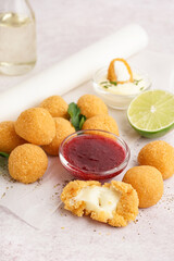 Paper with delicious fried mozzarella balls, sweet sauce and lime on light background