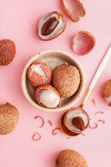Bowl with tasty litchi fruit and spoon on pink background