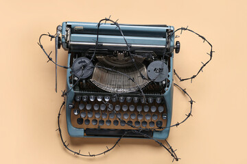 Vintage typewriter with barbed wire on beige background. Printing ban concept