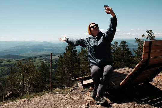 Young woman sitting up and posing cheerfully for a selfie on top of Tornik mountain in Serbia, surrounded by stunning nature. Travel blogger making video outdoor