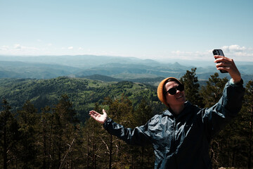 Female traveler taking selfie with breathtaking spring landscape in the background, standing confidently above the forest in Zlatibor, Serbia country. Travel blogger making video outdoor