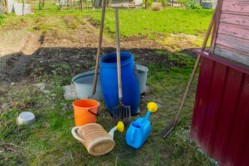 Garden buckets and watering cans of different colors in a suburban area near the wall of the house