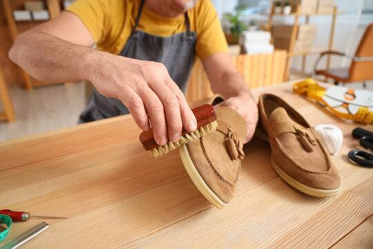 Mature shoemaker brushing shoe at table in workshop, closeup
