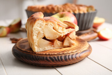Wooden board with piece of tasty homemade apple pie on light background