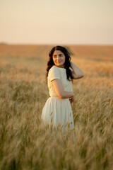 A young brunette walks in wheat fields at sunset in summer. Growing organic wheat and barley.