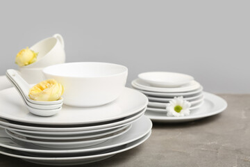 Simple tableware and flowers on table near grey wall