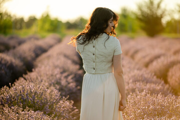A young brunette walks in wheat fields at sunset in summer. Growing organic wheat and barley.