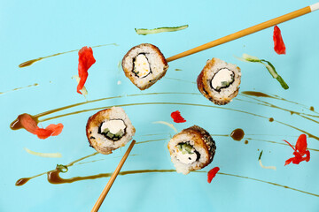 Tasty flying sushi rolls, soy sauce and chopsticks on blue background