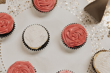 Top-down view of pink frosted cupcakes and white fondant cupcakes arranged on a lace paper doily...