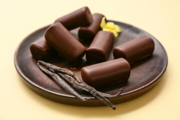 Plate with tasty chocolate glazed curd snacks with vanilla flavor on light yellow background