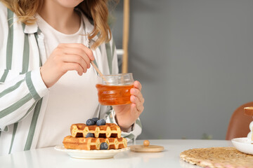 Woman adding sweet honey to sweet waffles in kitchen