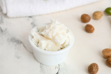Bowl of shea butter and nuts on light background