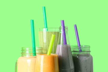 Glasses and mason jars of different fresh smoothie on green background