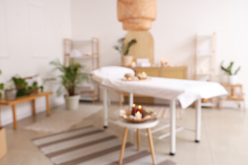 Blurred view of light spa salon with massage couch, burning candles and shelf units