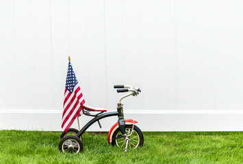 vintage tricycle with American flag on green grass with horizontal white background and room for copy