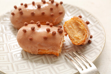 Plate with sweet eclairs on light  background, closeup