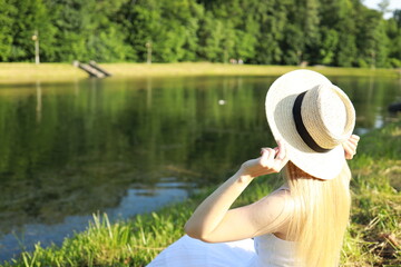 Woman in a white dress enjoying a sunny day by a serene lake surrounded by lush greenery