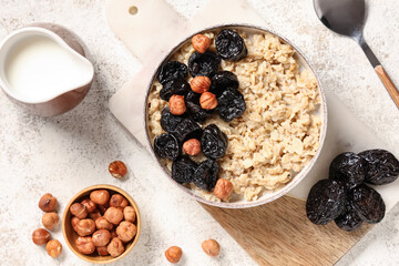Bowl of tasty oatmeal with prunes, hazelnuts and jug of milk on white grunge background