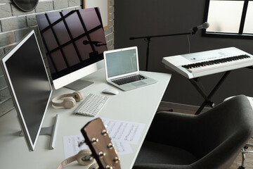Workplace with blank laptop, computer monitors and synthesizer in recording studio