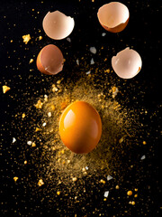 Obraz premium Cracked Egg Yolk in Midair with Shell and Golden Particles on Dark Background