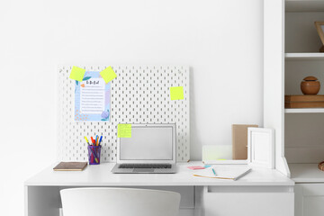 Workplace with blank laptop, pegboard and to-do list in office