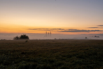 Morning fog shrouds high-voltage power transmission towers in rural area