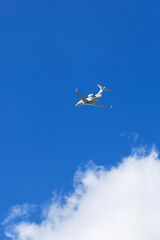 Private jet flying high in the blue sky above the clouds in Hostivice, Czechia