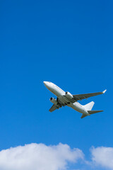 White passenger airplane flying high in blue sky over white clouds