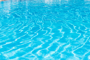 Clear blue water surface with small waves reflecting sunlight in swimming pool