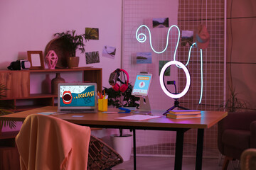 Podcaster's workplace with laptop, tablet computer and glowing neon lamp in dark studio