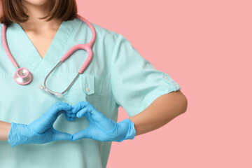 Female cardiologist with stethoscope showing heart gesture on pink background, closeup