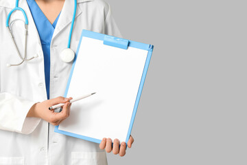 Female cardiologist with stethoscope pointing at clipboard on grey background, closeup