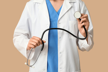 Female cardiologist with stethoscope on beige background, closeup