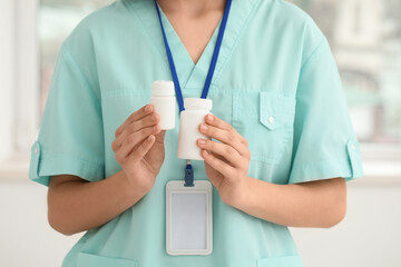 Female cardiologist with badge and jars of pills in clinic, closeup