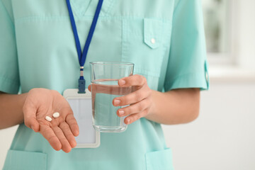 Female cardiologist with badge, cup of water and pills in clinic, closeup