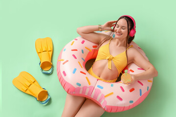 Female tourist in headphones with swim ring and flippers on green background, top view