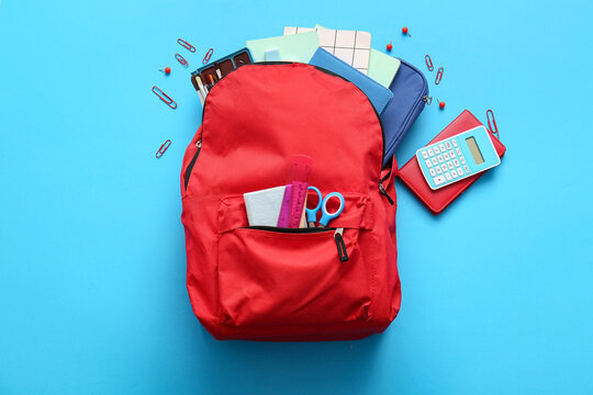 Red school backpack with different stationery supplies on blue background